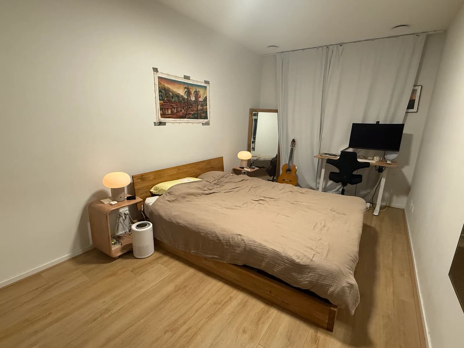 Bedroom as it is: a wooden bed with a beige duvet, a bedside table, a standing mirror and a desk in front of the curtain