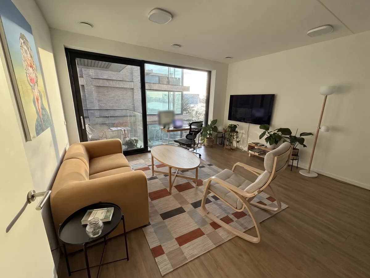 The same living room furnished with an ochre STOCKHOLM sofa, a POÄNG rocking chair, an oval wooden coffee table, a checked rug and a floor lamp