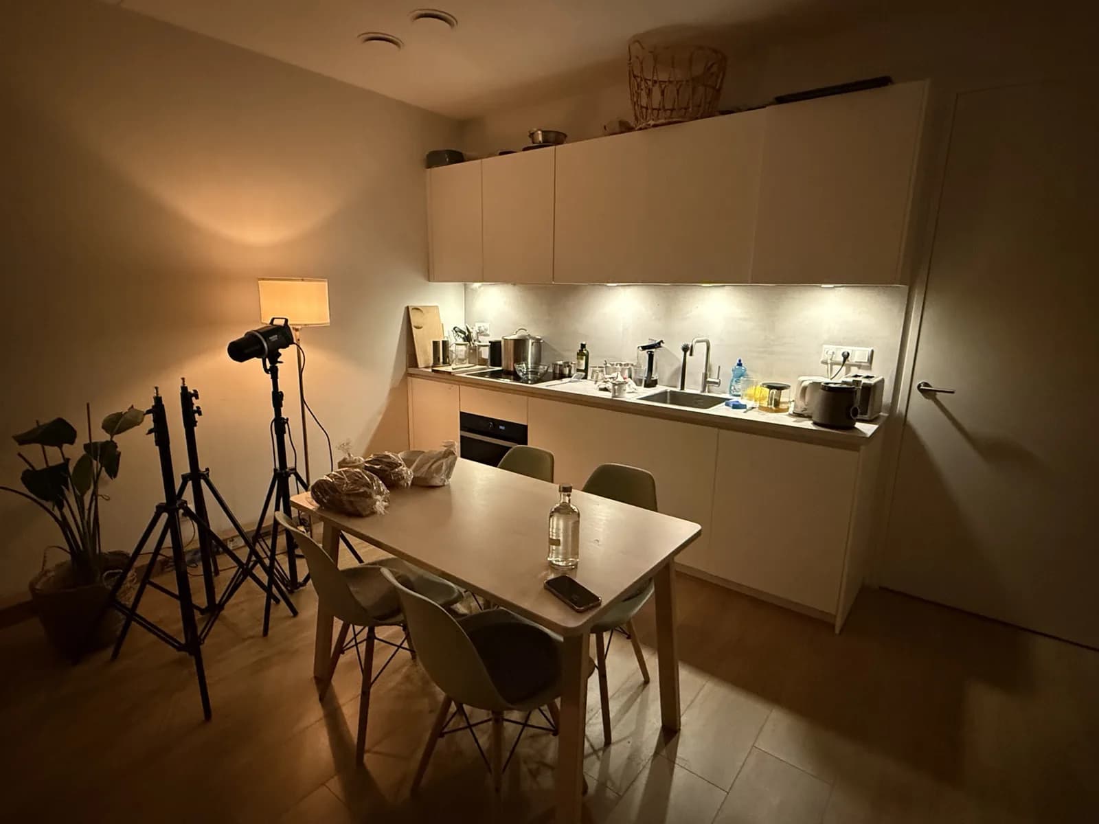 Kitchen as it is: a white kitchen along the wall, a light dining table with chairs and photo lights in the corner