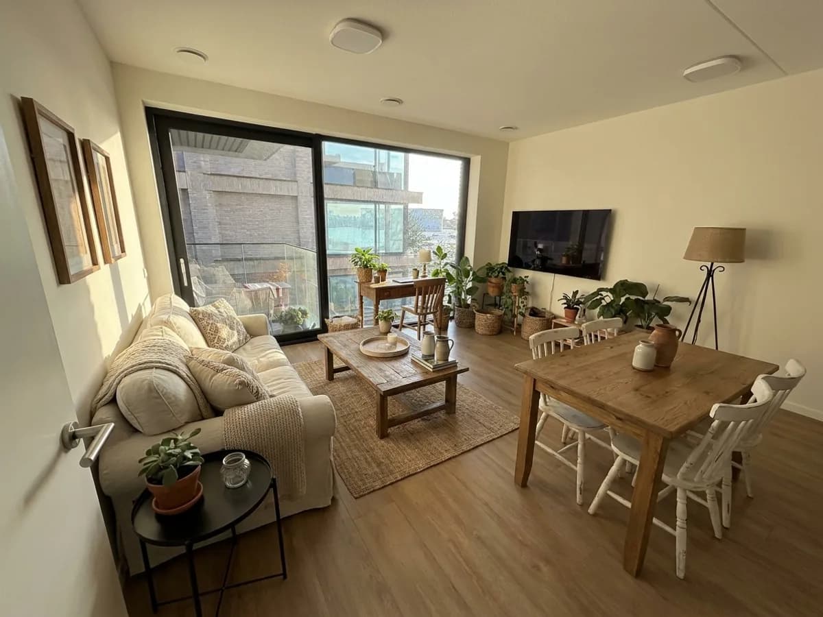 The same living room in farmhouse style: a linen sofa with throws, a wooden coffee table on a jute rug and a wooden dining table with white spindle chairs